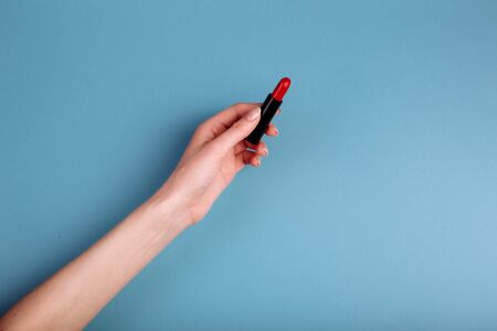 The womans hand is taking red lipstick. isolated On the blue backgroundの写真素材