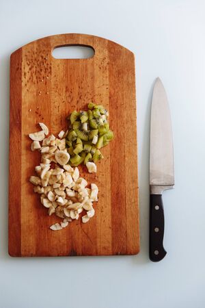 Fresh cut of banana and kiwi on wooden chopping board with knife. isolated on white, from above, flat lay..の写真素材