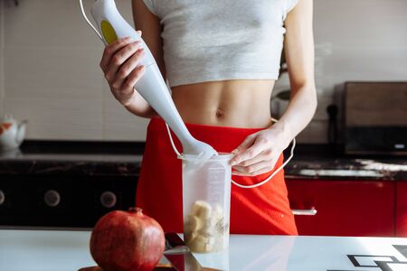 Woman with hand blender making sweet banana protein powder milkshake smoothie. protein shake after workout. sport nutrition diet after gym. Healthy lifestyle.の写真素材