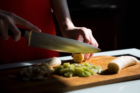 Woman's hands cutting fresh banana on the wooden board on the kitchen.の写真素材