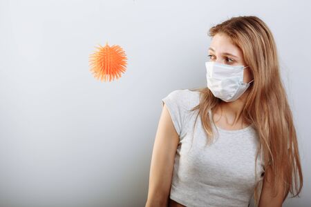Scared young woman in medical mask standing near covid-19 virus molecule. Concept of coronavirus and Asian flu panic.の写真素材