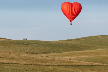 Hot air balloon in shape of heart is landing on the green field.の写真素材