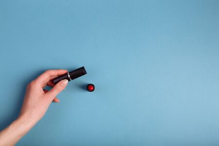 Lady's hand holding closed red lipstick isolated on blue background near to opened lipstick.の写真素材