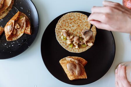 Woman's hand decorates pancakes with a fruits kiwi and banana. Black plate, white table.の写真素材