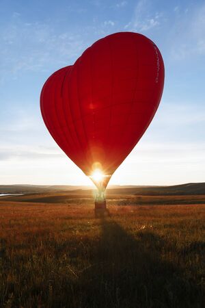 hot Red air balloon heart shape flying into sunset over valley landing or taking off.の写真素材
