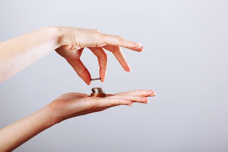 Woman's hand giving or taking golden coin to another hand on isolated white background, crisis concept.の写真素材