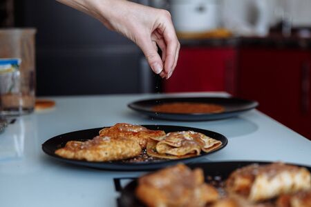 Pastry chef's hand decorates pancakes with a chocolate, fruits kiwi and banana. Black plate, white table.の写真素材