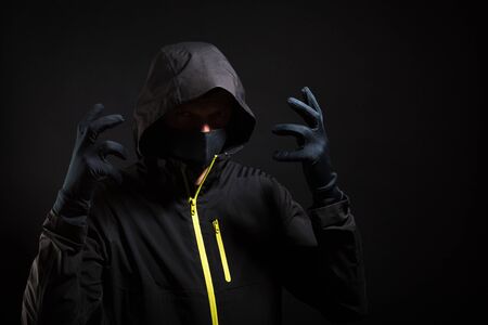 Masked thief is trying to scare you with raised arms isolated on black background.