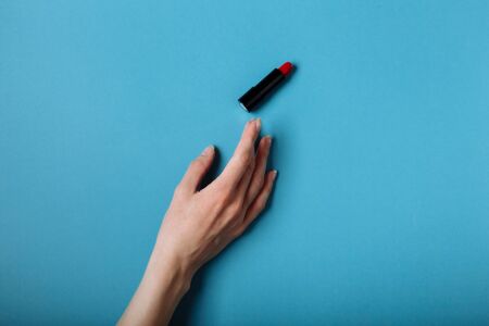 The woman's hand is taking red lipstick. isolated On the blue background.の写真素材