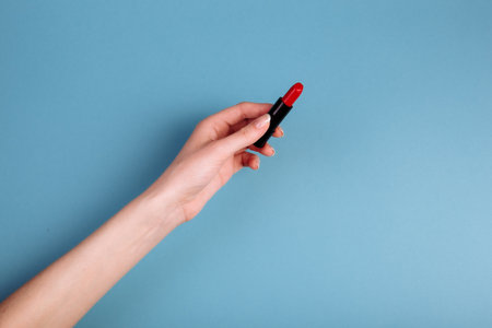 The woman's hand is taking red lipstick. isolated On the blue background.の写真素材
