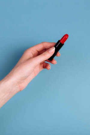 The womans hand is taking red lipstick. isolated On the blue backgroundの写真素材