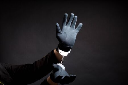 closeup of the hands of a burglar in black gloves with handcuffs on a black background.の写真素材