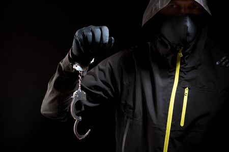 closeup of the hands of a burglar in black gloves with handcuffs on a black background.の写真素材