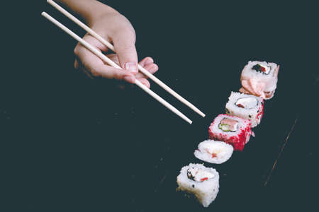 Female hand takes chopsticks sushi rolls with Chinese chopsticks. Lying on a black wooden board....