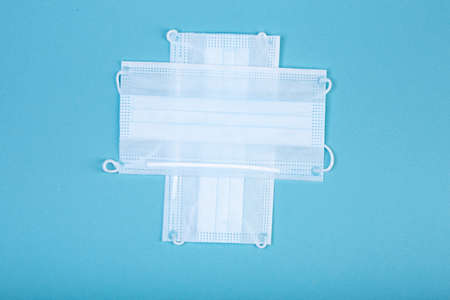 healthcare, medicine and charity concept: white cross symbol made from two white surgical masks for protection from  isolated on blue backgroundの写真素材