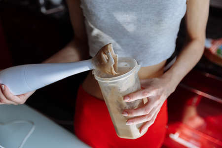 healthy eating, cooking, vegetarian food, dieting and people concept - close up of woman hand holding a blender for fruit shake at homeの写真素材