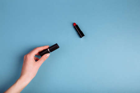 Ladys hand holding closed red lipstick isolated on blue background near to opened lipstickの写真素材
