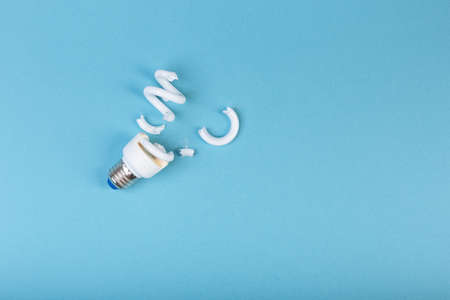 Broken fluorescent spiral tube lamp energy-saving lamp surrounded by dead ficus leaves on  blueの写真素材