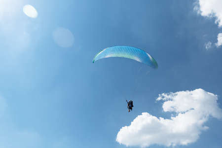 Blue Paraglider flying into the sky with clouds in a sunny day