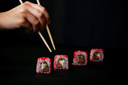 Female hand takes chopsticks california sushi rolls with Chinese chopsticks. Selective focus, black backgroundの写真素材