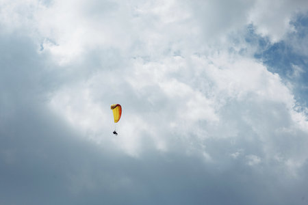 Yellow Paraglider tandem instructor with a tourist flying into the sky with clouds on a sunny dayの写真素材
