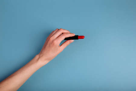 The womans hand is taking red lipstick. isolated On the blue backgroundの写真素材