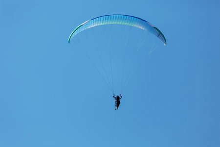 Blue Paraglider flying into the sky with clouds on a sunny day.の写真素材