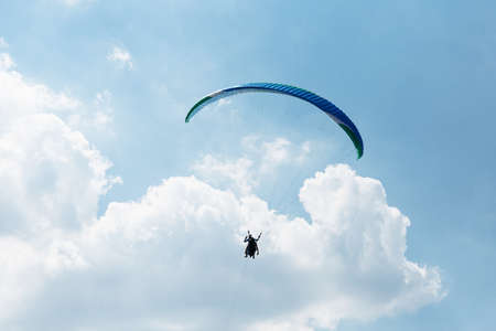 Blue Paraglider flying into the sky with clouds on a sunny dayの写真素材