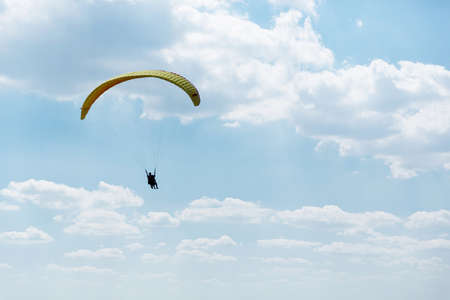 Yellow Paraglider flying into the sky with clouds on a sunny dayの写真素材
