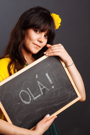 Latin brazil lady in a soccer clothes holding a small blackboard with Hello word on his native language isolated on gray backgroundの写真素材