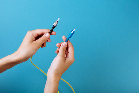 womans hands hold SC and FC connector fiber optic patch cord single mode on blue backgroundの写真素材