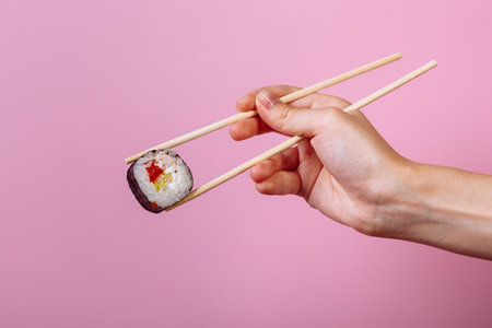 Tasty sushi roll maki with wooden chopsticks on pink background close up. Place for caption and textの写真素材