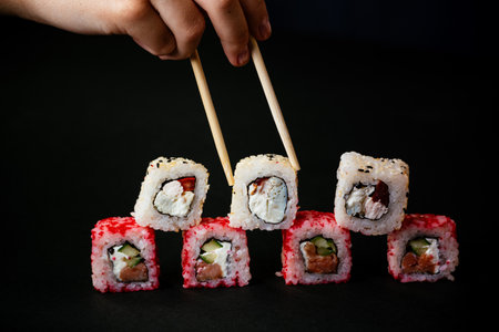 Female hand takes chopsticks california sushi rolls with Chinese chopsticks. Selective focus, black backgroundの写真素材