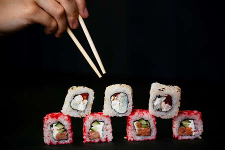 Female hand takes chopsticks sushi rolls with Chinese chopsticks. Lying on a black wooden board. View from aboveの写真素材