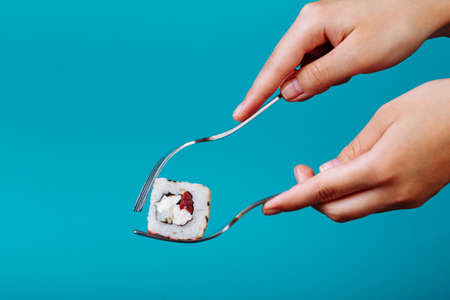 how to eat sushi roll with a fork, isolated on blue background. How to eat sushi without chopsticksの写真素材