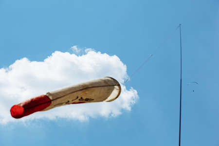 Blue Paraglider flying into the sky with clouds on a sunny day. the Wind cone is on the foregroundの写真素材