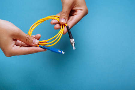 womans hands hold SC and FC connector fiber optic patch cord single mode on blue backgroundの写真素材