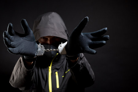 Thug or hucker in handcuffs and black clothes is arested. Concept: Crime because of crisis covid 19. isolated on black backgroundの写真素材