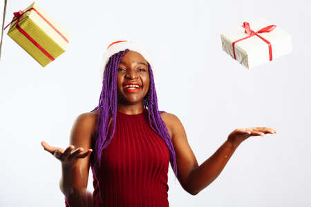 Beautiful Afro American woman is catching falling presents, looking at camera and smiling, isolated on white backgroundの写真素材