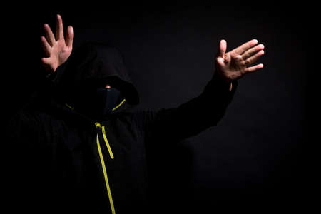 Masked thief is trying to scare you with raised arms isolated on black background