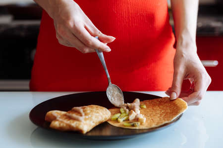 Womans hand decorates pancakes with a fruits kiwi and banana. Black plate, white tableの写真素材