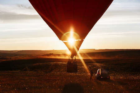hot Red air balloon heart shape flying into sunset over valley landing or taking offの写真素材