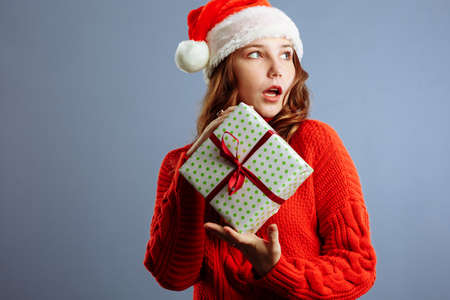 Happy europian Santa Woman is surprised and holding Gift Box for Christmas or New Year. Isolated on gray backgroundの写真素材