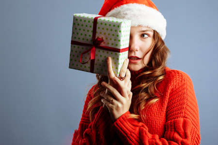 Happy europian Santa Woman is surprised and holding Gift Box for Christmas or New Year. Isolated on gray backgroundの写真素材