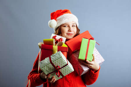 Beautiful white woman in a dress and Santa hat is catching falling presents, looking at camera and smiling, isolated on gray backgroundの写真素材