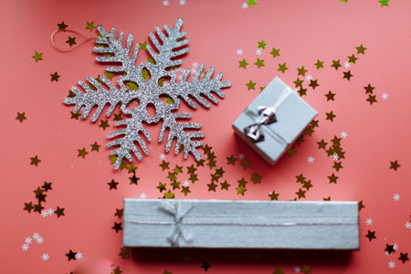 Silver snowflake and white textured gift boxes with ribbon bows surrounded by stars and snowflakes on a coral background, from above ..の写真素材