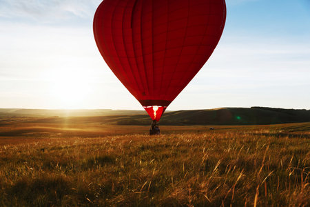 hot Red air balloon heart shape flying into sunset over valley landing or taking offの写真素材