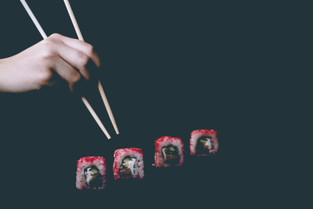 Female hand takes chopsticks california sushi rolls with Chinese chopsticks. Selective focus, black backgroundの写真素材