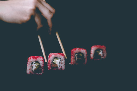 Female hand takes chopsticks california sushi rolls with Chinese chopsticks. Selective focus, black backgroundの写真素材