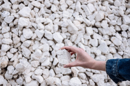 Hand holds a white chalkstone with a lot of stones on the backgroundの写真素材